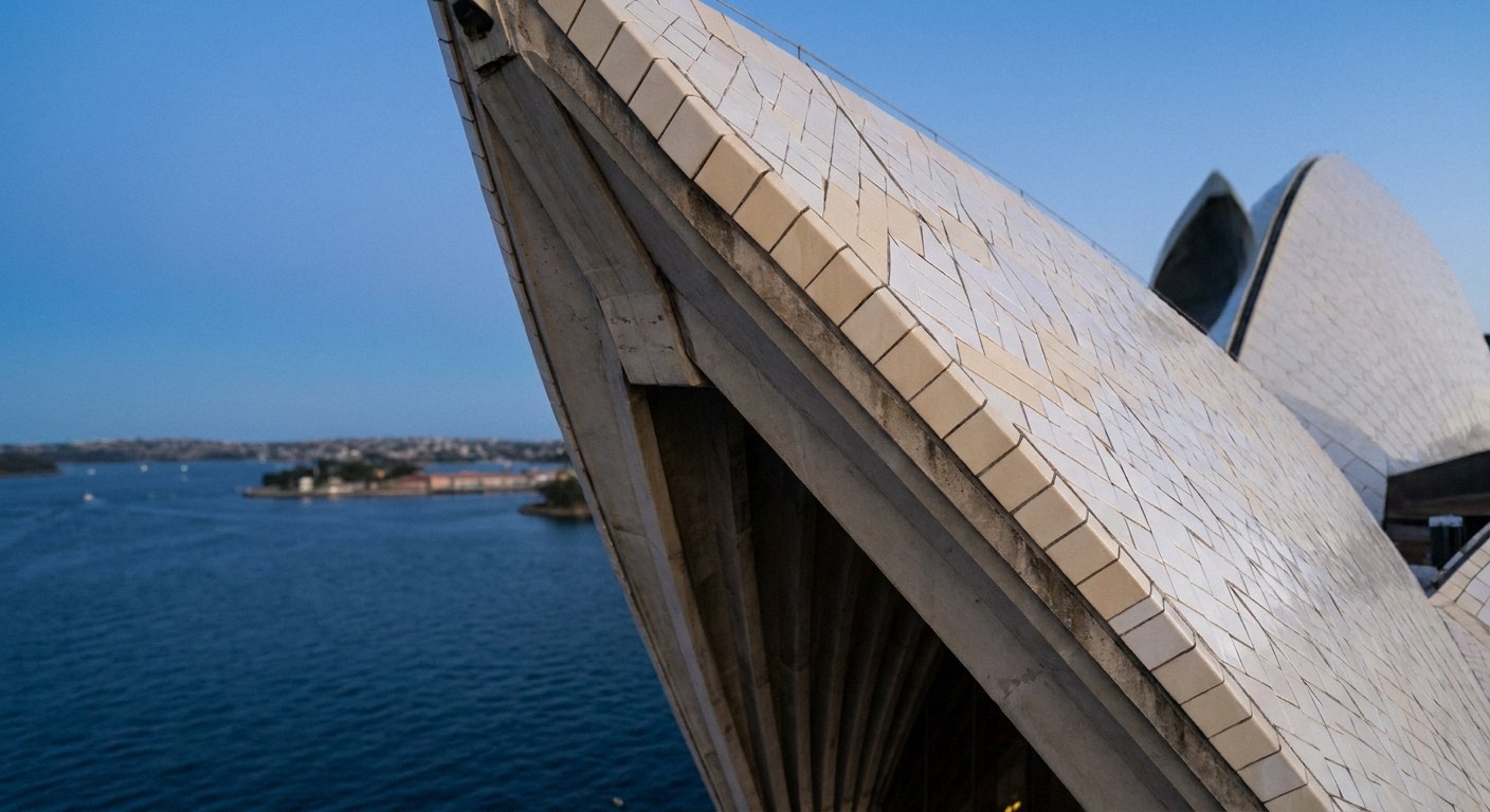 Close-up of a tiled, sail-shaped roof overlooking a blue harbor and distant shoreline under a clear sky